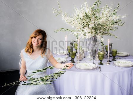 Sitting Bride With Olive Branch In Hands  And Wedding Decorations For Banquet With Sakura, Candles A