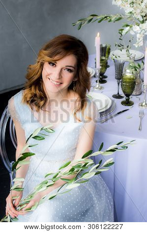 Sitting Bride With Olive Branch In Hands  And Wedding Decorations For Banquet With Sakura, Candles A