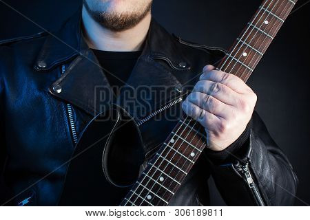 Photo of a biker in black leather jacket with skull rings holding electric guitar on black background.