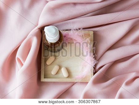 Brown Glass Bottle With Essential Oil Or Creme, Vitaminen And Pink Feather On The Texture Fabric. To