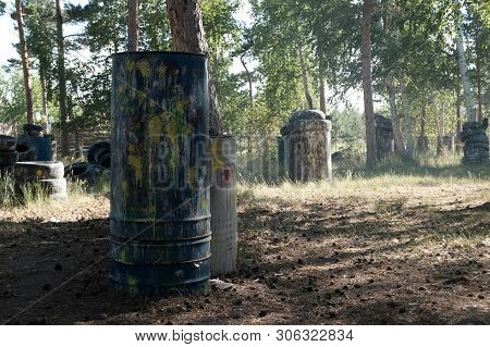 Iron Barrels In The Foreground With Multi-colored Blots And Smudges From Shots From The Paintball We