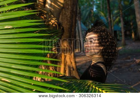 Asian girl looks through the palm leaves.