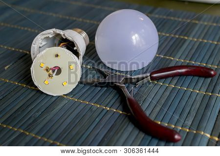 Faulty, Disassembled Led Household Lamp With A Burnt Led Element Is On The Table Next To The Pliers