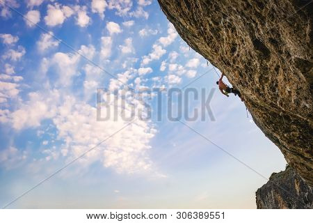 Athletic Man Climbs An Overhanging Rock 8c-9a Category Against Blue Cloudy Sky With Rope. Sport Clim