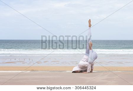 Woman Yogi Doing The Pigeon Pose On A Stone Cube On The Beach With The Sea In The Background