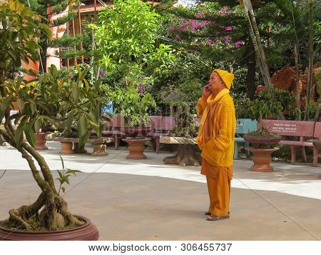 Vietnam, Dalat, January 8, 2015. A Buddhist Monk In Yellow Clothes Is Listening To Something On A Ce