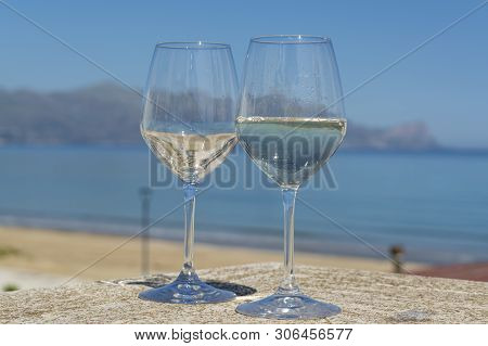 Two Wine Glasses With White Wine Served On Outdoor Terrace Witn Blue Sea And Mountains View On Backg