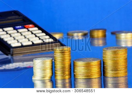 A Stack Of Metal Coins Accountant And A Calculator On A Blue Background. A Coin Is A Monetary Sign M