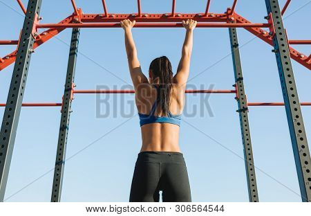 Rear View Of Fit Young Female Doing Pull Ups Exercises On Crossbar Outdoors. Athlete Woman Training 