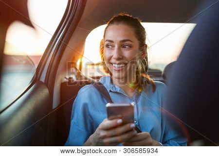 Young woman with smartphone on the back seat of a car