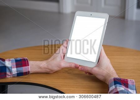 Man Sitting At Wooden Table And Looking At Digital Tablet Computer Device With White Blank Screen. M