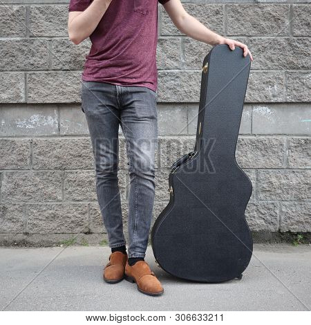 Man Put His Foot On A Hard Guitar Case. Hard Case For Electric Guitar. Man Dressed In Jeans Holding 