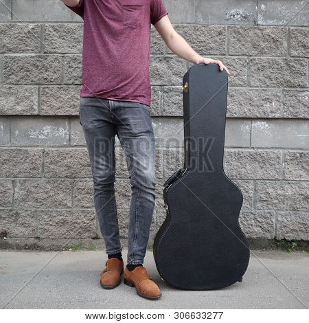 Man Put His Foot On A Hard Guitar Case. Hard Case For Electric Guitar. Man Dressed In Jeans Holding 