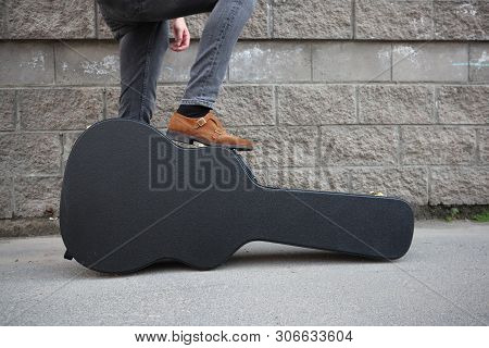 Man Put His Foot On A Hard Guitar Case. Hard Case For Electric Guitar. Man Dressed In Jeans Holding 