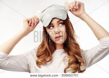 Thoughtful Relaxed Young Woman Has Curly Hair, Wears Eyemask, Slumber Suit, Looks Away Intently And 