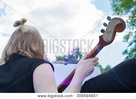 Girl At A Street Concert Outdoors Playing The Contrabass, A Musical Instrument, Looking At A Noteboo