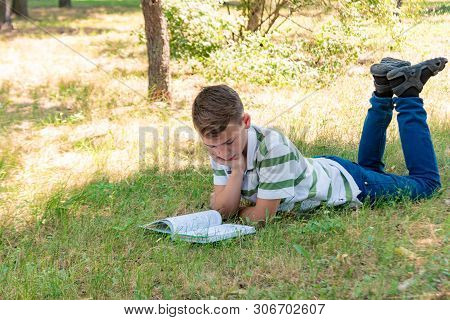 The Boy Lies In The Park On The Grass And Is Studying In Nature, Education And Science, The Book Is 