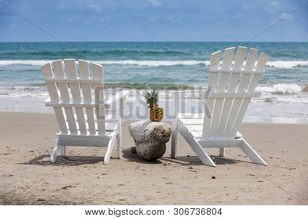 Empty White Wooden Chairs At A Paradisiac Beach On The Tropics In A Beautiful Sunny Day