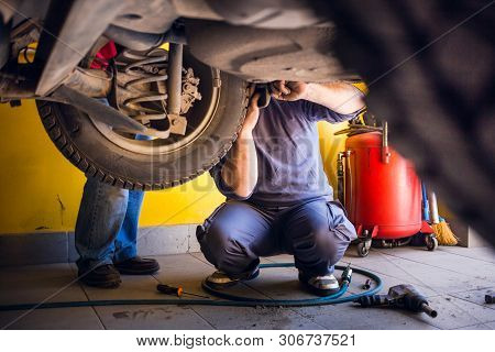 Photo Of  Car Mechanics Fixing The Car. Inside The Car Shop. View From Under The Car