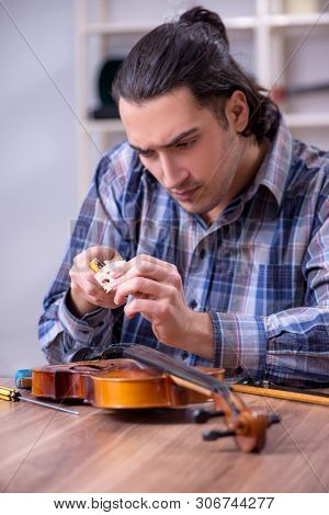 Young handsome repairman repairing violin