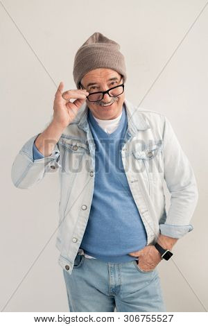 Happy mature man in casualwear standing on white background and looking at you through eyeglasses