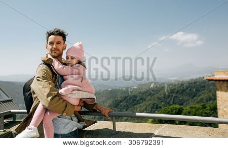 Outdoor Horizontal Image Of Father Holding His Daughter Looking At Mountains And Sea View At Sunny D