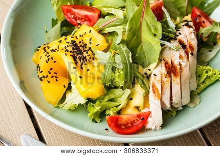 Salad With Grilled Chicken, Mango, Lettuce, Avocado, Tomatoes, Arugula, Cheese Sause On A White Plat