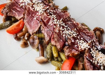 Sliced Medium Rare Roast Beef With Pickles, Cherry Tomatoes, Mushrooms On A White Plate On Wooden Ba