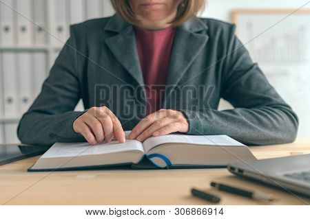 Businesswoman Reading Book At Office Desk, Searching For The Business Realted Information