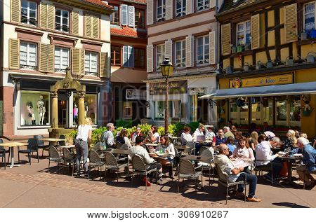 Colmar, France - April 18, 2019. People Eating In The Street Restaurant In Front Of The Medieval Hou