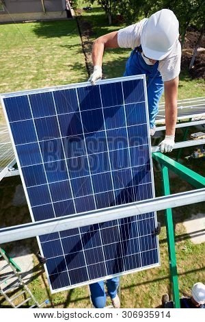 Two Mounters Installing Solar Panels On Green Metallic Carcass. Wearing Blue Uniform, Protective Hel