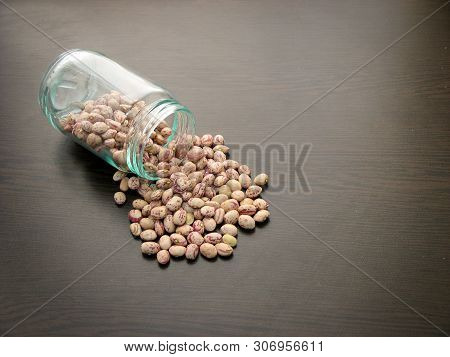 Pinto Bean Seeds Glass Jar. Pinto Bean Seeds Are Poured From A Glass Jar On Brown Wooden Surface. Cl