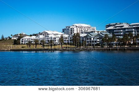 Harbourside Condominium Apartment Housing With Grass Frontage, Blue River Against Blue Sky