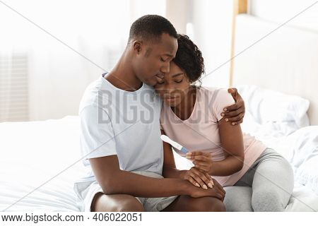 Upset Black Couple Holding Negative Pregnancy Test, Husband Hugging His Depressed Wife, Bedroom Inte