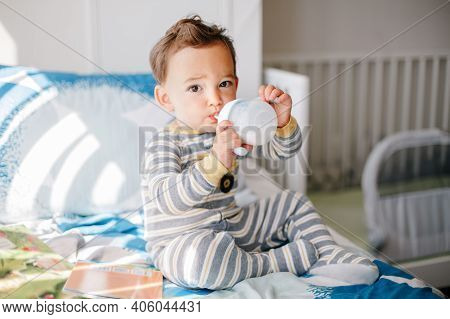 Cute Adorable Caucasian Kid Boy Sitting On Bed Drinking Milk From Kids Bottle. Healthy Eating Drinki