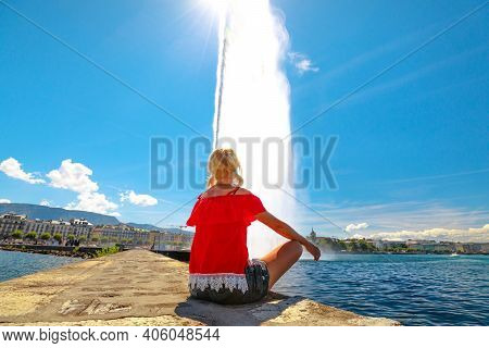 Blonde Tourist Woman Sitting A Pier, Looking Jet Deau Fountain Which Projects Its Water Spray 140 Me