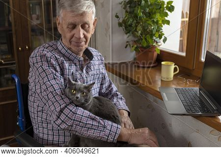 An Elderly Man Is At Home, Hugging His Favourite Cat Sitting On His Lap. Attachment To The Old Man's