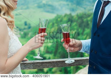 Glasses With Red Champagne Drink In Bride And Groom Hands. Happy Newlyweds Drinking. Loving Couple C