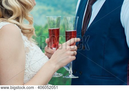Glasses With Red Champagne Drink In Bride And Groom Hands. Happy Newlyweds Drinking. Loving Couple C