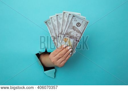 A Woman Hand Appears In The Hole In Torn Paper And Squeezes Dollar Bills. The Concept Of Alimony Pov