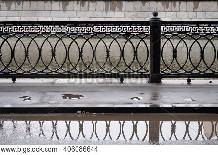 A Puddle On The Asphalt And The Reflection Of A Metal Lattice In It On The Embankment Of The Vodootv