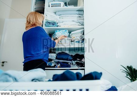 Back View Of A Woman Organizing A Wardrobe, Holding Towels In Her Hands And Putting Them On A Shelf.