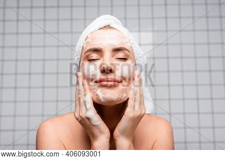Happy Woman With Closed Eyes Applying Foam Cleanser In Bathroom