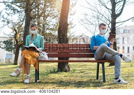 Woman and man in social distancing sitting on bench in park