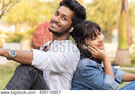 Young Teenage Friends Enjoying Listening To Favorite Song Or Music By Sitting Back To Back At Colleg