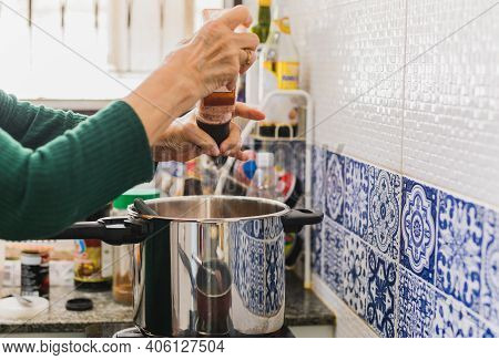 Senioe Woman Adding Himalayan Salt In A Pot On A Stove In The Kitchen.