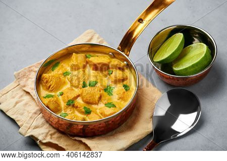 Chicken Korma In Copper Pan On Gray Concrete Table Top. Indian Cuisine Meat Curry Dish With Coconut