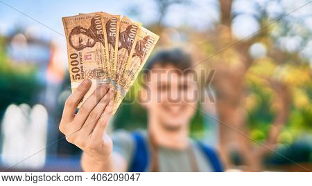 Young caucasian tourist man smiling happy holding hungarian forint banknotes at the city.