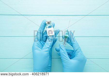 Bottle With Vaccine Against Covid 19 And Syringe In Hand Of Researcher Wearing Gloves On Blue Backgr