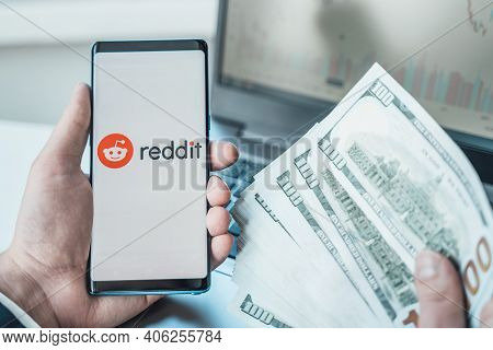 Russia Moscow 02.02.21 Mobile Phone With Logo Of Reddit Traders, Money,dollars In Hands.community Of